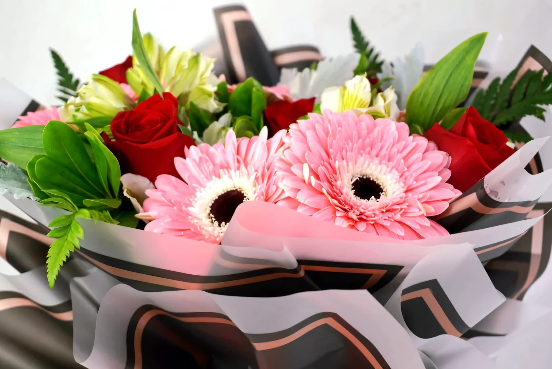 Ramo de gerberas rosas y rosas rojas envuelto en papel premium