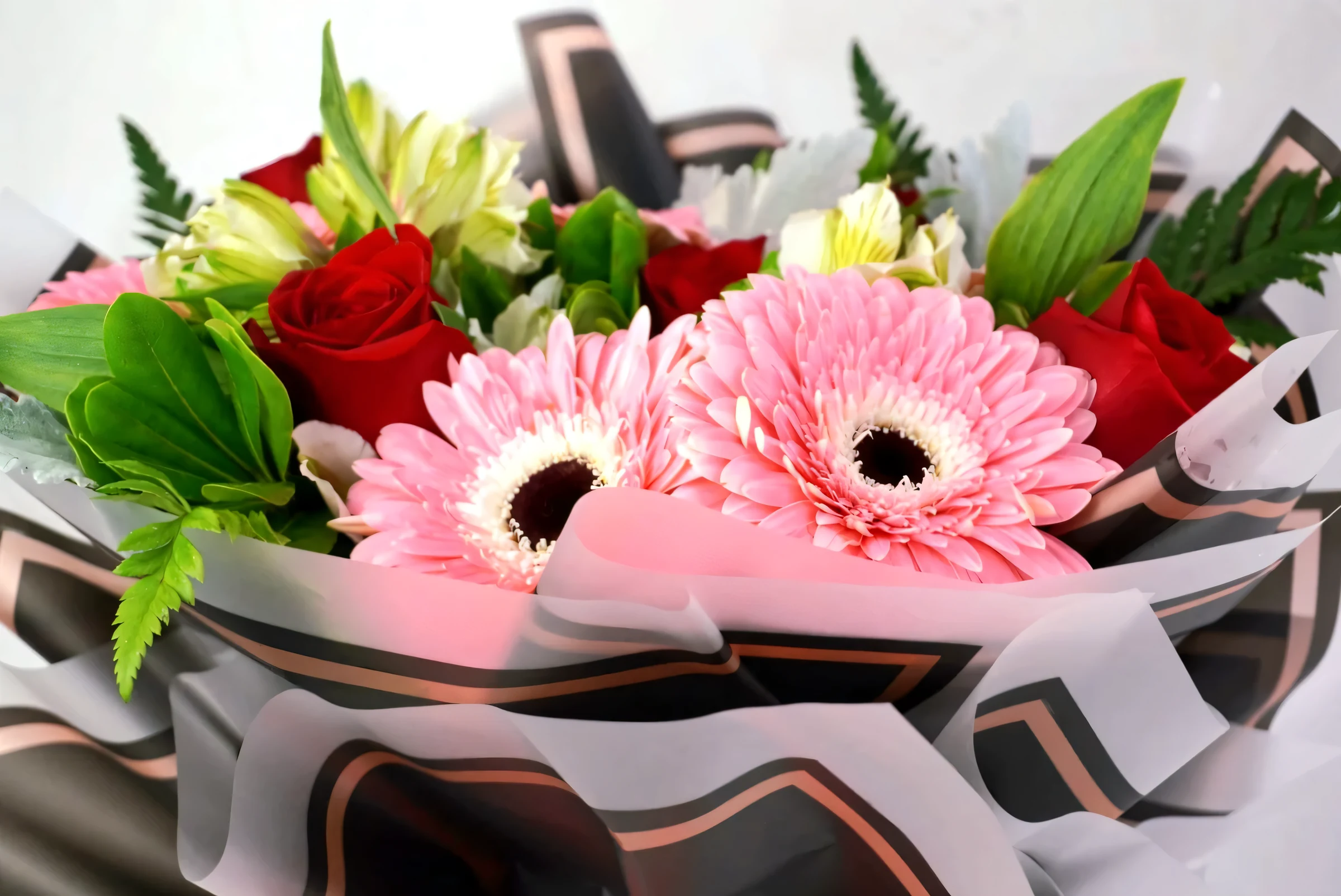 Ramo de gerberas rosas y rosas rojas envuelto en papel premium