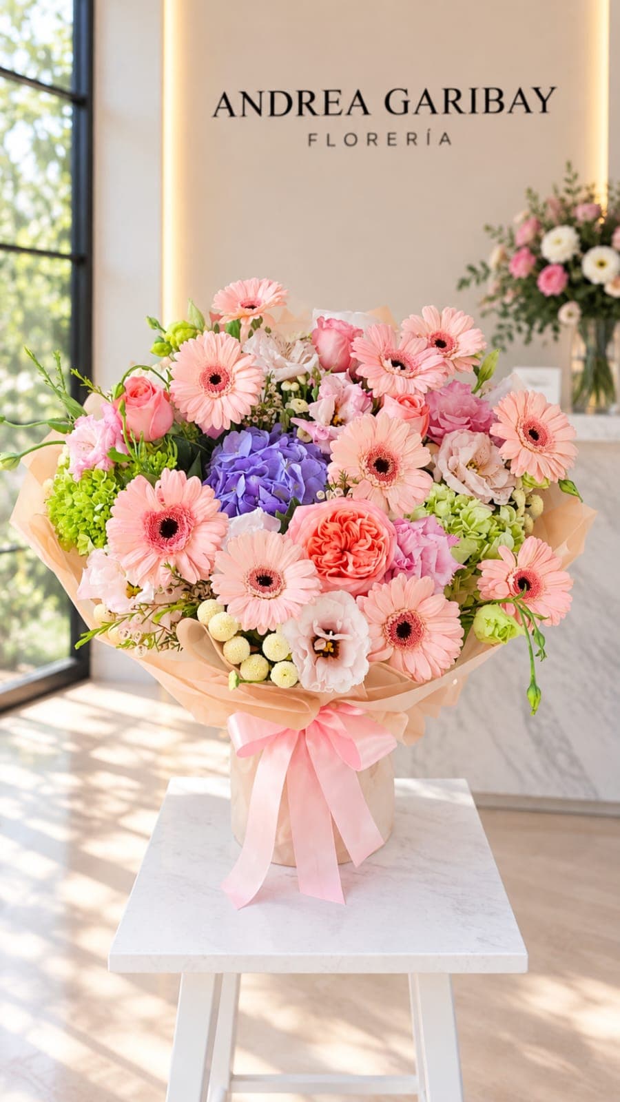 Ramo Lía con gerberas rosa pastel, rosas rosadas, hortensias lavanda y verdes, lisianthus y envoltura durazno con listón rosa.
